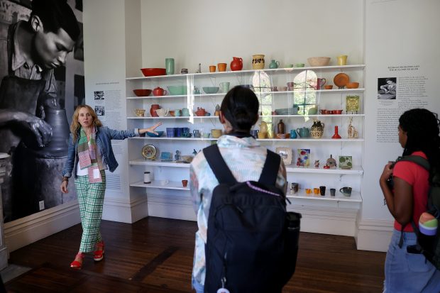 Liesl Olson, director of the Jane Addams Hull-House Museum, gives a tour of the "Radical Craft" exhibit to students from the University of Chicago Laboratory School on Oct. 2, 2024. Displayed on the shelves are varying types of ceramic arts created by Mexican migrants, among them Jesús Torres, pictured on wall.(Chris Sweda/Chicago Tribune)