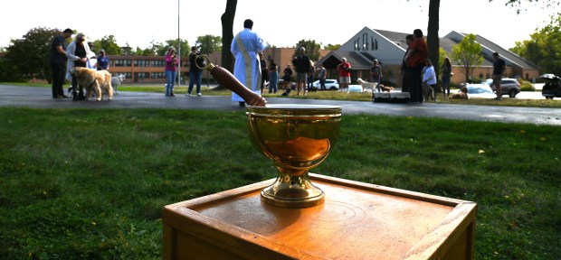 Holy water in the foreground. In white wardrobe, Deacon Kevin Garvey of Deerfield offers narrative at the pet blessing at Holy Cross Church in Deerfield on the front lawn of rectory, The House on The Hill on Oct. 5, 2024. (Karie Angell Luc/Lake County News-Sun)