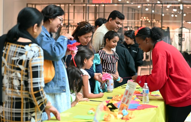 Right, Kyra Barber of Waukegan, representing Dandelion Gallery and Studio of Waukegan, assists families with crafts on Oct. 12, 2024 at the Hispanic Heritage Celebration at Hawthorn shopping mall in Vernon Hills. (Karie Angell Luc/Lake County News-Sun)