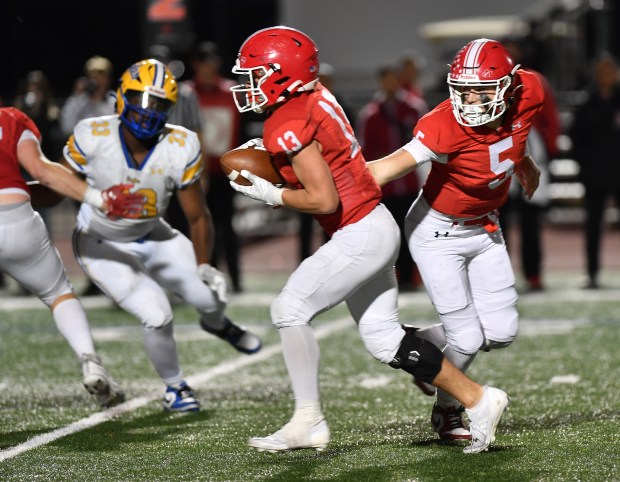 Naperville Central quarterback Sebastian Hayes (right) hands of to Aiden Clark (13) during a game against Sandburg on Friday, Oct. 18, 2024 in Naperville...(Jon Cunningham/for The Naperville Sun)