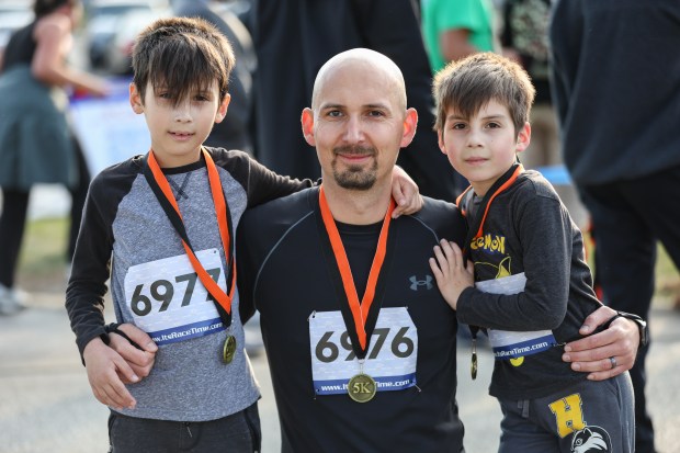 Kamil Kowalski, center, kneels for a photo with his sons Luke, 9, right, and Logan, 8, left, after finishing the 11th annual Harvest Hustle 5k in Niles on Saturday, Oct. 12, 2024. The race raises funds for the Niles Family Services Food Pantry. (Troy Stolt / for the Pioneer Press)