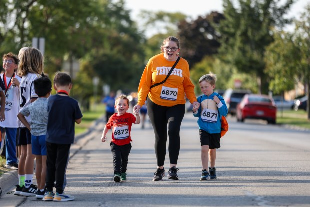 Megan Newman, center, of Niles holds hands with sons Alex, 4, right, and George, 6, left as the finish the 11th annual Harvest Hustle 5k in Niles on Saturday, Oct. 12, 2024. The race raises funds for the Niles Family Services Food Pantry. (Troy Stolt / for the Pioneer Press)