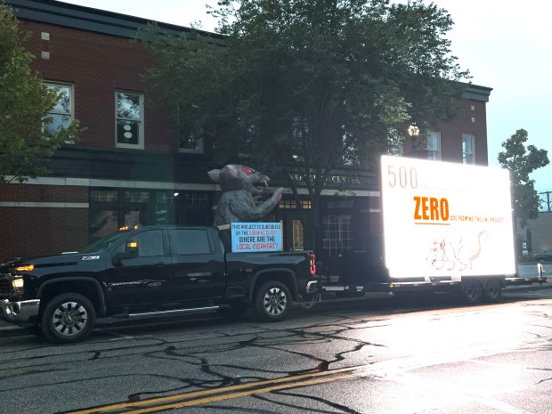 A truck and trailer parked across the street from Valparaiso City Hall before the Oct. 14, 2024, Valparaiso City Council meeting display an inflatable rat and signage warning about the dangers of hiring unskilled craftspeople and labor for The Linc apartments and garage project downtown. (Philip Potempa/for Post-Tribune)