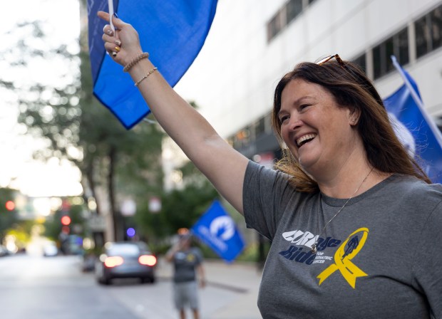 Karen Sporny waves a flag at the start of the five-day, four-state CUREage Bike Ride, Oct. 6, 2024, to raise funds for pediatric cancer research in memory of her daughter, Megan, who biked two years ago. (Brian Cassella/Chicago Tribune)