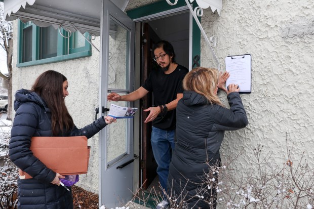 Alison Ernst, left, hands Will Leon a flyer for her husband, then-congressional candidate Nikhil Bhatia, outside his home in Oak Park on Dec. 31, 2023, as signing agent Michelle Rocco notarizes an affidavit affirming Leon previously signed a petition to put Bhatia on the ballot. (Eileen T. Meslar/Chicago Tribune)