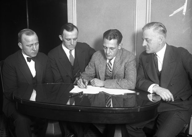 On Nov. 22, 1925, less than 24 hours after his last game with the Fighting Illini, Harold "Red" Grange, second from right, signed a contract to play pro football with the Chicago Bears at the Morrison Hotel in Chicago. Surrounding Grange as he signed are Bears managers Edward Sternaman, from left and George Halas, as well as Grange's agent, Charles C. Pyle, right. (Chicago Tribune historical photo)