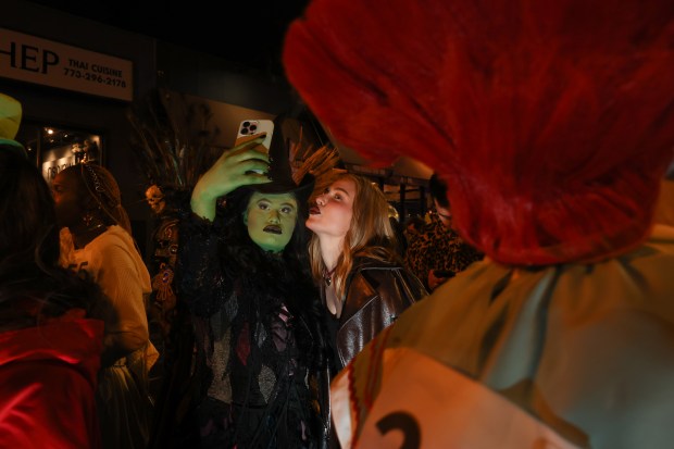 Mikey Shock, left, and Alina Orlova take photographs while dressed as witches for the Haunted Halsted Halloween Parade in the 3200 block of North Halsted Street, Oct. 31, 2024, in Chicago. (John J. Kim/Chicago Tribune)