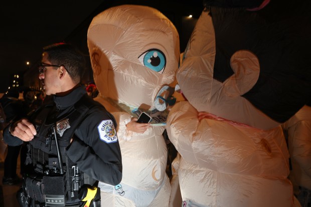 Two people wearing inflatable baby costumes talk closely next to a police officer during the Haunted Halsted Halloween Parade in the 3200 block of North Halsted Street, Oct. 31, 2024, in Chicago. (John J. Kim/Chicago Tribune)