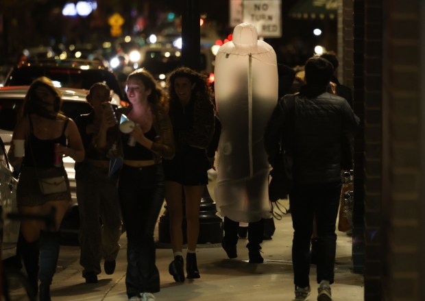 A group of women walk past a man wearing a condom costume in the 800 block of West Belmont Avenue, Oct. 31, 2024, in Chicago. (John J. Kim/Chicago Tribune)