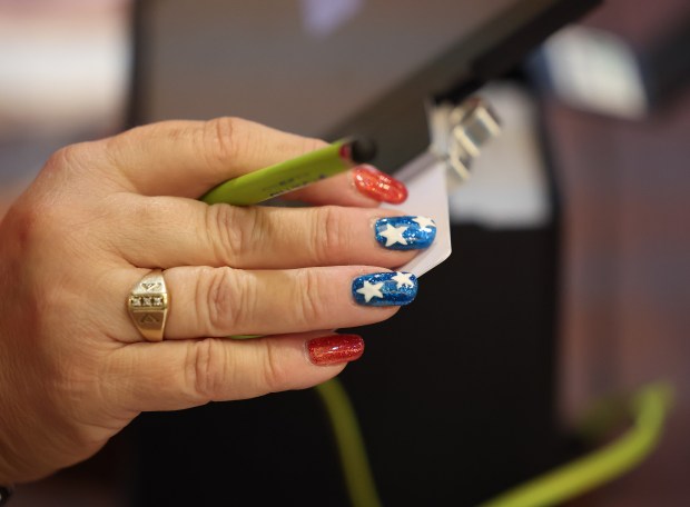 Lead election judge Cathy Vitale-Sweeney' patriotic nails as she checks people in to vote early at the Arlington Heights Village Hall, Oct. 28, 2024. Vitale-Sweeney said she's been an election judge for 25 years and said this year's turnout is the highest. This facility has the second highest early voters in suburban Cook County after Orland Park. (Stacey Wescott/Chicago Tribune)