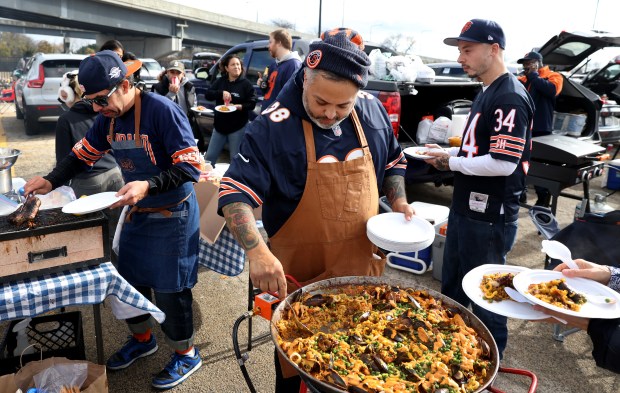 Chef Marcos Asencio (center) dishes out squid, shrimp, and chorizo paella as fellow chefs Alex Martinez (left) and Oliver Poilevey (right) prepare food during a tailgate with friends and acquaintances in the 31st Street parking lot before a game between the Chicago Bears and the New England Patriots at Soldier Field on Nov. 10, 2024. The three colleagues and friends are Bears season ticket holders. (Chris Sweda/Chicago Tribune)