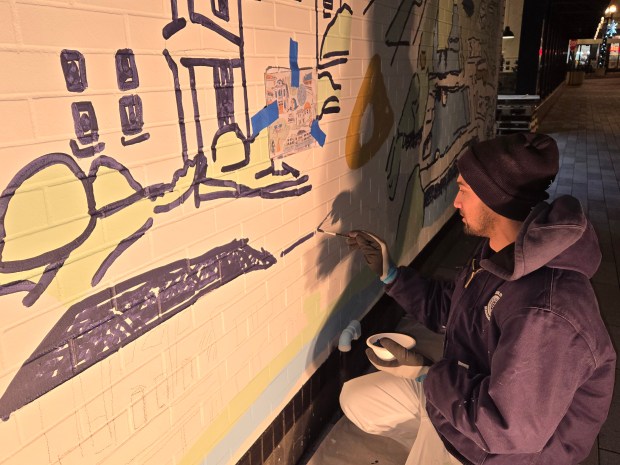 Artist Joel Feliciano replicates a coffee mug design by artist Ashley Klockenga on a wall of Dream Hall facing DuPage Court in downtown Elgin. Because of other commitments, Feliciano did most of the work at night, he said. (Gloria Casas/The Courier-News)