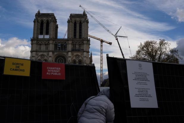 A pedestrian tries to get a peek at the forecourt of Notre-Dame cathedral in Paris, Wednesday, Nov. 20, 2024. (AP Photo/Louise Delmotte)