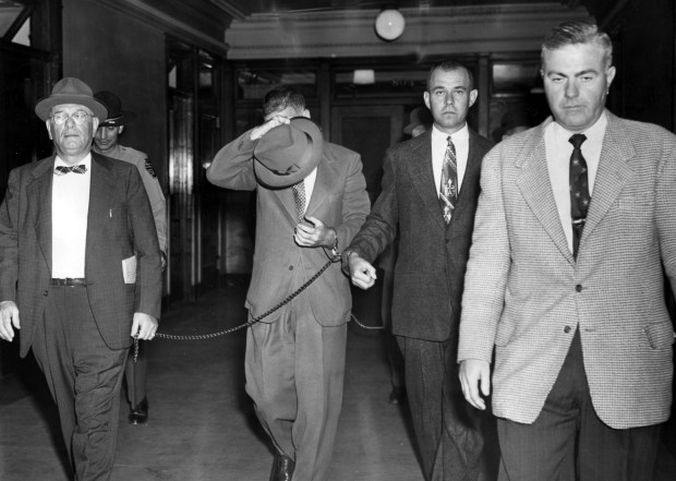 Former Illinois state auditor of public accounts Orville Hodge, with his face covered, walks out of the U.S. Marshal's office in Chicago on Oct. 10, 1956. Hodge was convicted on charges of embezzling state funds. (Chicago Tribune)