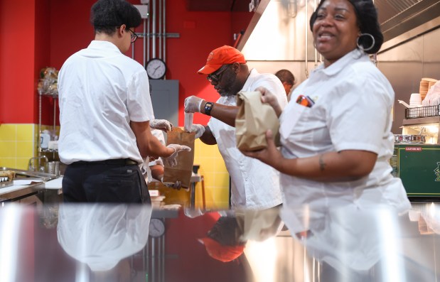 Workers Bryant Wynne, center, and Korey Lee, left, bag food orders in the kitchen at Mac's Deli with supervisor Jesseka Leggett, right, during the eatery's soft opening on Nov. 14, 2024, in Chicago. It's staffed by clients of the Haymarket Center through its workforce development and job training program. (John J. Kim/Chicago Tribune)