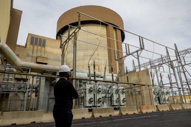 An employee looks up at the Unit 2 containment structure for the nuclear plant at the Braidwood Clean Energy Center in Braceville on Nov. 13, 2024. Below it are main power transformers and auxiliary transformers, which receive offsite electricity and send off the electricity generated by the plant. (Tess Crowley/Chicago Tribune)