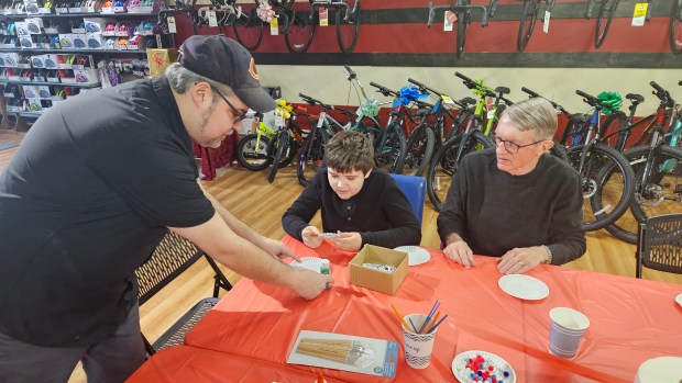 Prairie Path Cycles co-owner Mike Maravilla, left, shows Colter Bennion, 10, and his grandfather John Wahlers of Winfield how to make ornaments out of recycled bike parts Saturday at Prairie Path Cycles in Batavia. (David Sharos / For The Beacon-News)