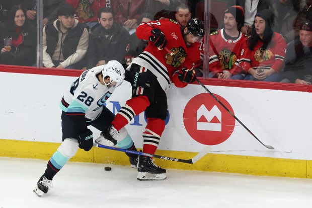 Kraken defenseman Joshua Mahura (28) and Blackhawks left wing Patrick Maroon (77) battle for control of the puck in the first period at the United Center in Chicago on Dec. 19, 2024. (Terrence Antonio James/Chicago Tribune)