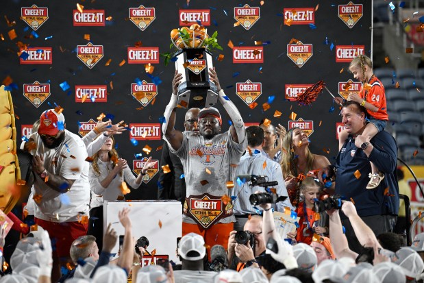 Illinois running back Josh McCray, center, raises the championship trophy after his team's win over South Carolina in the Citrus Bowl as coach Bret Bielema, right, looks on Tuesday, Dec. 31, 2024, in Orlando, Fla. (AP Photo/Phelan M. Ebenhack)