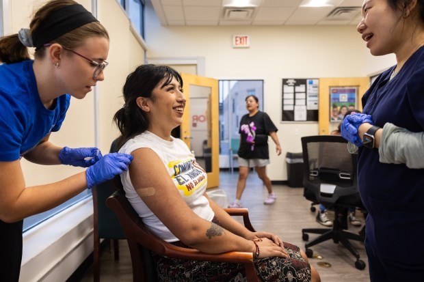 Angelica Glogowski, a UIC student and member of the Outbreak Response Team, left, administers an mpox vaccine to Iselle Jimenez, center, while Minseung Chu, clinical assistant professor at UIC College of Nursing converses with the pair at a vaccine event at Calor, a Latino nonprofit catering to people with HIV, in the Humboldt Park neighborhood on Oct. 30, 2024. (Tess Crowley/Chicago Tribune)