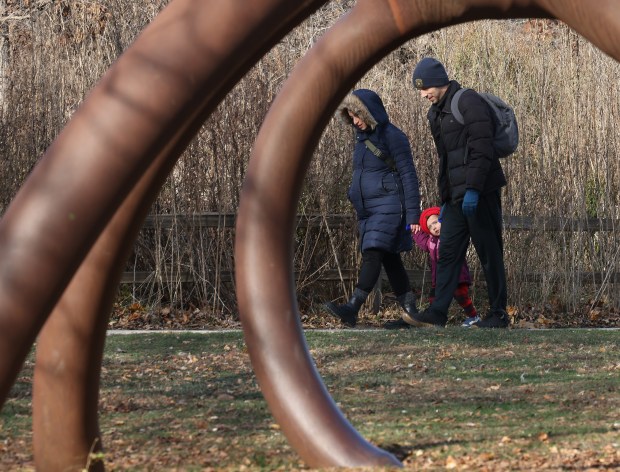 Bundled in winter clothing, Sasha Klyachkina and Nate Dick walk hand-in-hand with their daughter, Bella, 2, past a sculpture outside the Peggy Notebaert Nature Museum on Nov. 30, 2024. (John J. Kim/Chicago Tribune)