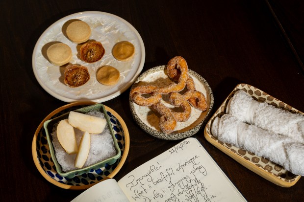 The spicebush funnel cake, a plate of Grandma's shortbread, pecan potato pie and maple candy, iced Oriana's pear, and a warm towel and a guest book are seen at Feld restaurant in Chicago on Dec. 18, 2024. (Tess Crowley/Chicago Tribune)