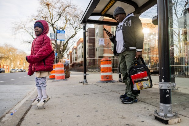 Iseoluwa Adegbite, 7, left, and mother Omotunde Adegbite, right, wait for the CTA 4 bus at East 63rd Street and South Cottage Grove Avenue in Chicago's Woodlawn neighborhood on Dec. 10, 2024. (Tess Crowley/Chicago Tribune)