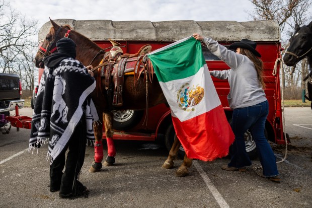 Nicole Garcia, right, and husband Saul Candelaría, from Club Los Vaqueros Unidos, prepare their horse named Alazan for the Archdiocese of Chicago's annual horseback pilgrimage in honor of Our Lady of Guadalupe. (Tess Crowley/Chicago Tribune)