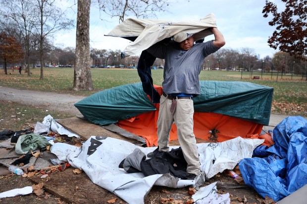 Angel Torres puts on some extra layers of clothing while living in a scattered homeless encampment in Chicago's Humboldt Park on Dec. 4, 2024. He doesn't know how his belongings got in disarray, but suspects police might be responsible. Torres grew up in the neighborhood and has been homeless for 2 years. (Chris Sweda/Chicago Tribune)