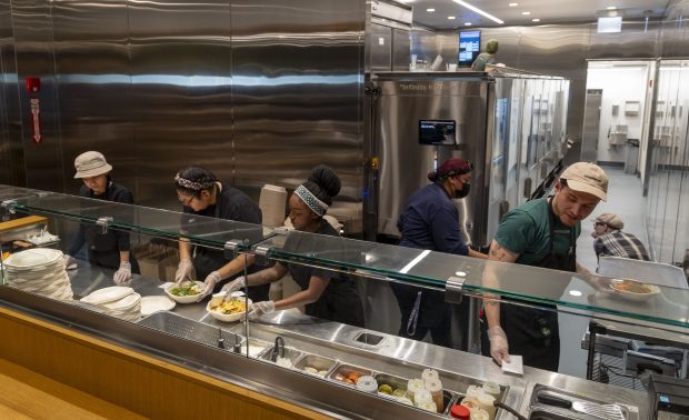 Sweetgreen workers add the final ingredients as salads come off the new Infinite Kitchen robotic system during a test run, Dec. 15, 2024, at Willis Tower. (Brian Cassella/Chicago Tribune)