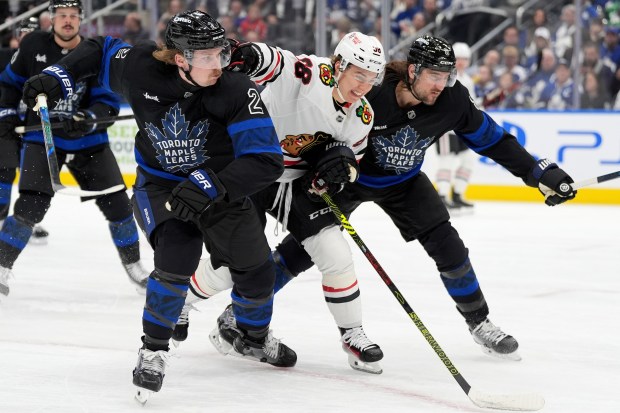 Chicago Blackhawks center Connor Bedard (98) shoves Toronto Maple Leafs defenseman Simon Benoit (2) as Maple Leafs defenseman Chris Tanev, front right, pursues as they vie for position during first-period NHL hockey game action in Toronto, Monday, Dec. 2, 2024. (Frank Gunn/The Canadian Press via AP)