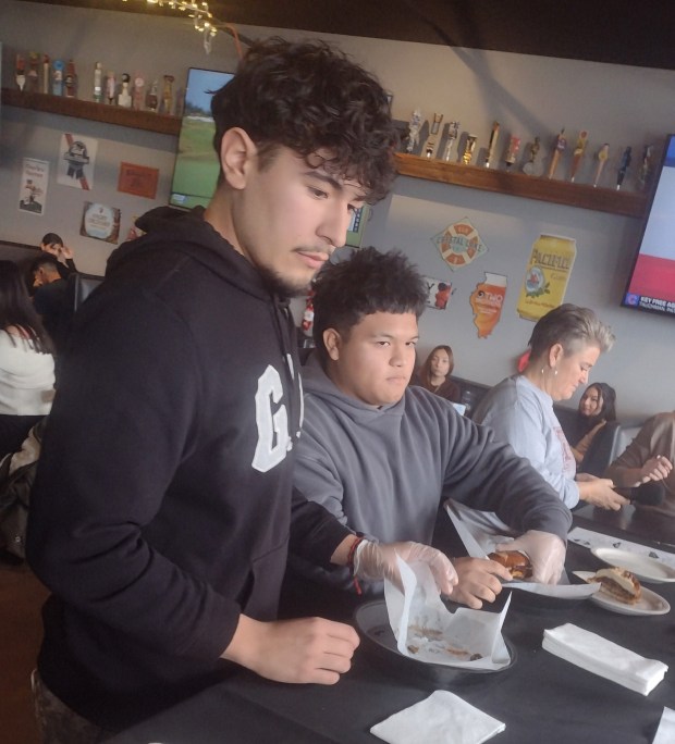 Budding chefs Geraldo Depaz, right, and Mario Perez present their Sweetness Burger to a panel of four judges Dec. 6, 2024 at the Chicago Street Pour House in Elgin. The duo's burger bested four other burgers to win a challenge set up by the restaurant for seniors taking part in the culinary arts program at Elgin High School. (Mike Danahey/for Courier-News)