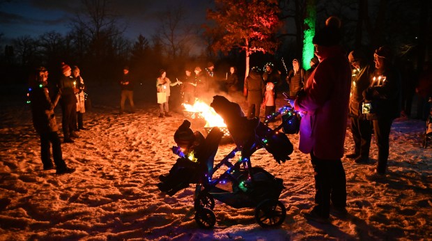 Left, Meridith Clement of Glencoe, FGBT trustee, addresses the audience. In the foreground is an illuminated stroller with parent Mariah Cunnick of Winnetka and children Ava Scovil, 2, and sibling Charlie Scovil, 1, at the ninth annual Winter Solstice Trail of Lights event and parade on Dec. 20, 2024 in Glencoe at Shelton Park. (Karie Angell Luc/Pioneer Press)