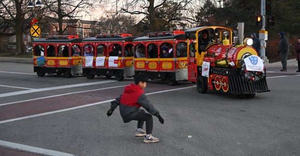 As the kiddie train rounds the corner, a youngster reaches for a piece of parade candy on Nov. 30, 2024 at the Holiday in the Park and Parade in downtown Glenview. (Karie Angell Luc/Pioneer Press)