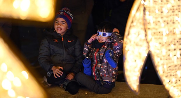 From left, Payton Evans and River Coon, both 5 and kindergartners from Northbrook, take turns seeing snowflakes made from festive glasses at Illuminate Northbrook on Nov. 22, 2024 in downtown Northbrook. (Karie Angell Luc/Pioneer Press)