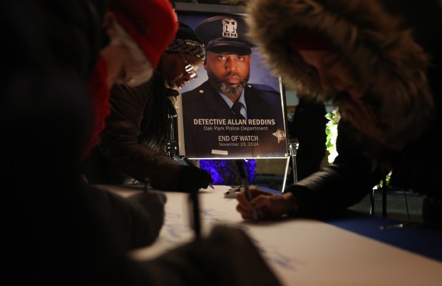 Mourners write notes of condolence next to a portrait of Oak Park police Detective Allan Reddins before a vigil in his memory at the Oak Park Village Hall Friday, Dec. 6, 2024. Reddins was fatally shot while responding to a bank robbery call on Nov. 29. (John J. Kim/Chicago Tribune)