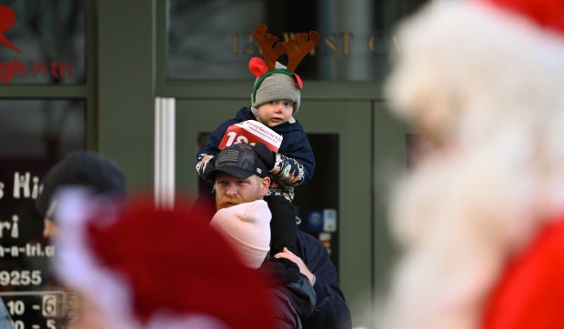 In his red rose, Van Smith, 3, of Arlington Heights, seems to be curious looking at Santa and Mrs. Claus along Campbell Street while sitting on the shoulder of his father Blake Smith. Taken at the Rotary Santa Run on Dec. 7, 2024 in downtown Arlington Heights. (Karie Angell Luc/Pioneer Press)