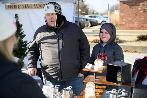 Zax Weaver, 10, one half of the brother duo who make up the Lake Brothers Wish Company, and his father Brian speak with visitors to their booth at the Chesterton Holiday Market on Saturday, Dec. 7, 2024. (Kyle Telechan/for the Post-Tribune)