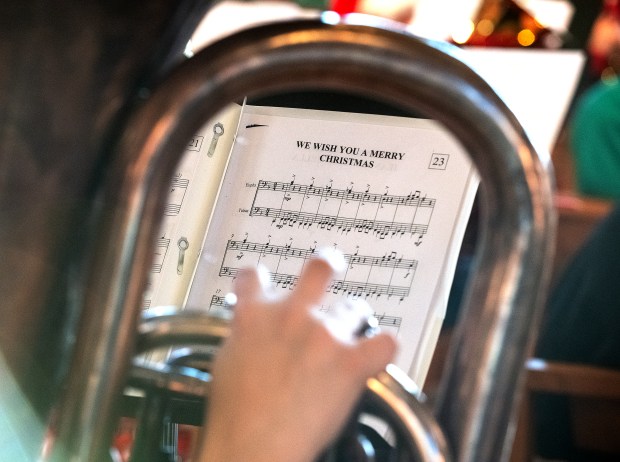 Christmas carol sheet music is seen through the bends of one of the more than 80 instruments that played during the TubaChristmas concert held in the Chapel of the Resurrection at Valparaiso University in Valparaiso, Indiana, on Sunday, Dec. 8, 2024. (Andy Lavalley/for the Post-Tribune)