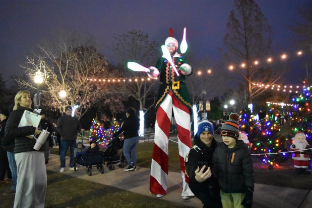 A woman and child take a selfie in front of the juggling stilt walker during Oak Lawn's Santa on the Green Dec. 7, 2024. (Jesse Wright/for the Daily Southtown)