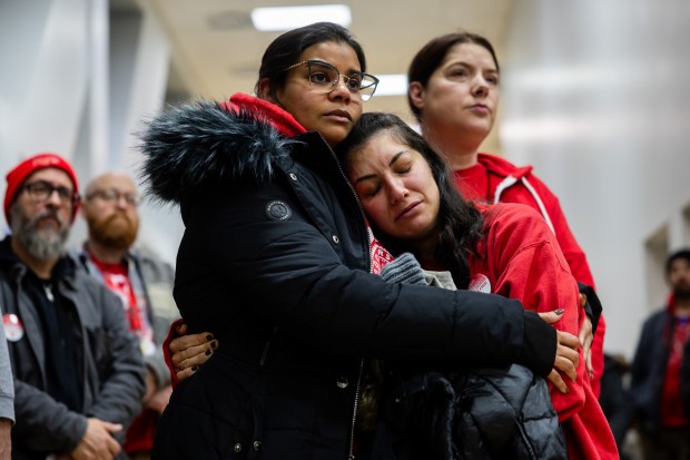 Acero Schools fourth-grade teacher at Carlos Fuentes Elementary Vicki Stamatakos, right, is hugged by second-grade teacher at Carlos Fuentes Elementary School Subhana Khaja, left, as they listen to people speak out against the closure of seven Acero schools during the charter network's board of directors meeting at Idar Elementary on Dec. 11, 2024. (Tess Crowley/Chicago Tribune)