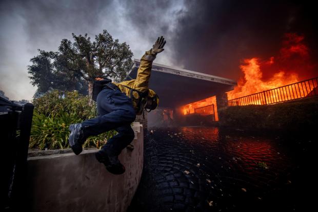 A firefighter jumps over a fence while fighting the Palisades Fire in the Pacific Palisades neighborhood of Los Angeles, Tuesday, Jan. 7, 2025. (AP Photo/Ethan Swope)