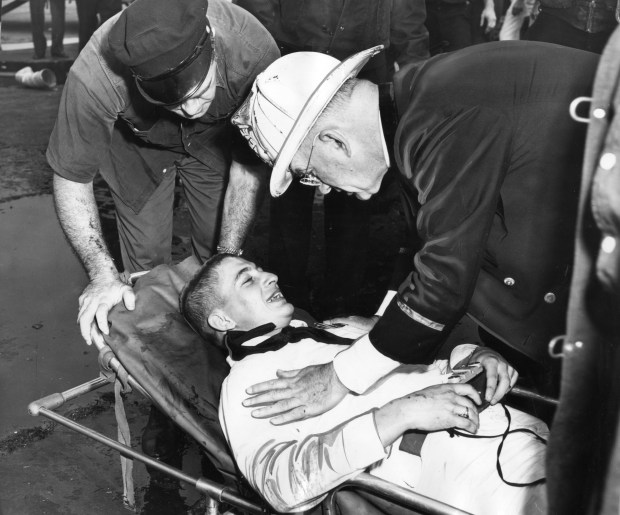 Kenneth McAdoo, 20, a sailor from Eldorado, Kansas, still clutches his camera as he smiles at fire department Chaplain William Gorman after being rescued from the July 17, 1955 plane crash at Midway Airport. (Chicago Tribune historical photo)