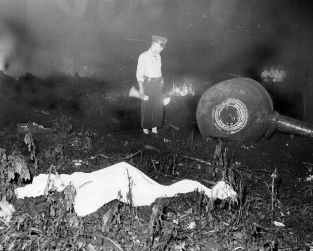 A policeman with a megaphone stands near the landing gear of the crashed Trans World Airlines plane in a cornfield just before dawn as a victim lies covered in a sheet in the foreground on Sept. 1, 1961. (Chicago Tribune historical photo) 