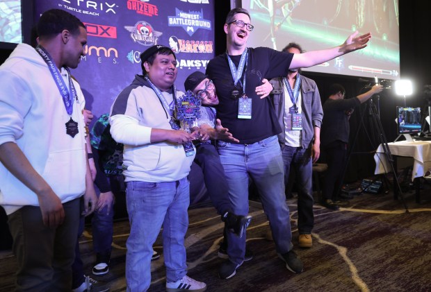 James Martinez, center left, holds the championship trophy as competitors Jose Dominguez, center, and Jacob Tranaude smile for cameras at the conclusion of the Marvel vs. Capcom 2 video game tournament during Frosty Faustings XVII at the Westin Chicago Lombard on Jan. 24, 2025. (John J. Kim/Chicago Tribune)