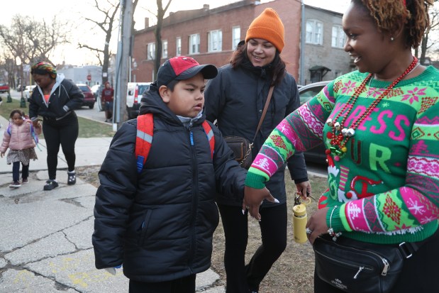 Beatrice Garcia, center, hands off her son, JoAngel Tapia, 7, to special education classroom assistant Jeannie Carrasquillo outside Henderson Elementary on Dec. 18, 2024. (Antonio Perez/Chicago Tribune)