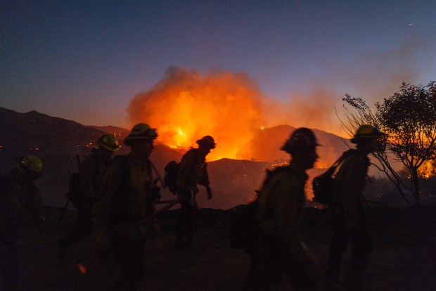 Firefighters work while smoke rises because of the growing Palisades fire in Los Angeles, California, on Jan.11, 2025. (Ali Matin/Middle East Images/AFP/Getty Images)