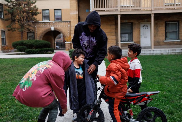 Lawrence Flowers, 21, gives his jacket to Alejandro Yovera, 4, while he plays with other migrant children, Nov. 25, 2024, in their Washington Park apartment complex.(Armando L. Sanchez/Chicago Tribune)