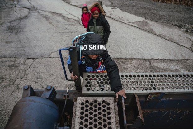 Jeremiah Johnson, 8, climbs up a small ladder on the side of a parked freight train Nov. 16, 2022, in Hammond, Indiana. Many mornings children who walk to school need to find a way of climbing over or under the train to make their classes on time. (Jamie Kelter Davis / for ProPublica)