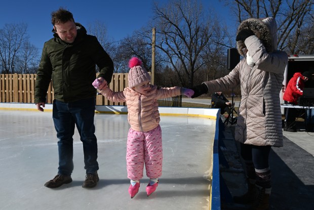 It's really bright outside on a sunny midday at a breezy 26 degrees. From left, parents Robert and Melissa Sell of Third Lake help their daughter Hannah Sell, 3, skate at the third annual Skate in the Park in Grayslake on Jan. 18, 2025. (Karie Angell Luc/Lake County News-Sun)